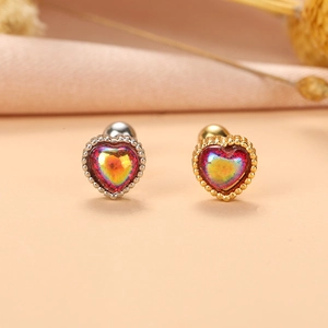 Détail de boucles d'oreilles cœur en argent et or avec pierres irisées sur tissu rose