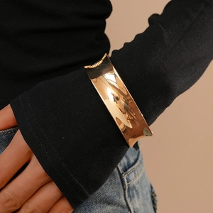 Minimalist wide gold cuff bracelet worn over a black sleeve for a stylish layering look