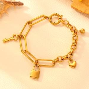 Detailed view of a gold-toned stainless steel link bracelet with key, lock, and bead charms