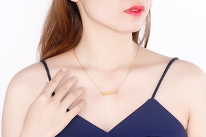 Detail of golden bar necklace with blue rhinestone pendant worn on a female model