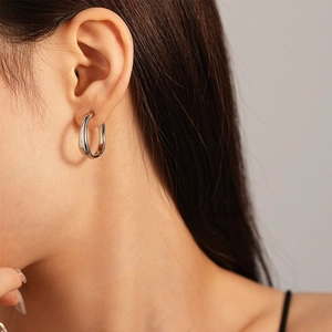 Gros plan d'une boucle d'oreille créole en U argentée minimaliste portée par un mannequin