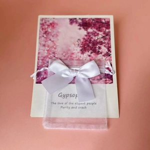 White organza gift bag with satin ribbon bow on pink background with cherry blossoms