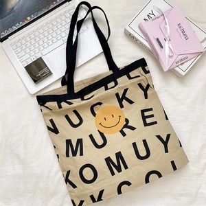 Detail of canvas tote bag with yellow smiley face print and black handles on desk