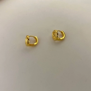 Detailed close-up of small golden huggie hoop earrings with polished finish on gray background