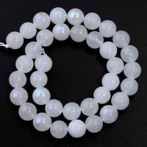 Macro detail of white moonstone beads with iridescent blue sheen on dark background