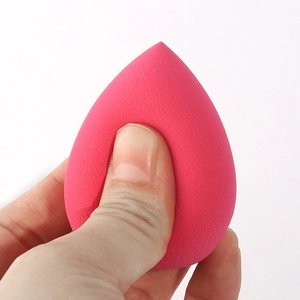 Soft magenta teardrop makeup sponge being pressed to demonstrate high elasticity and rebound