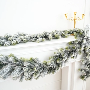 Detail of flocked Christmas garland with snow effect on a white mantel with gold candles