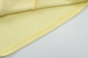 Macro detail of the light yellow vest hem featuring professional overlock stitching seams
