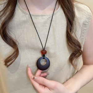 Close-up of retro Zen-style necklace with black ring pendant and amber bead on a model