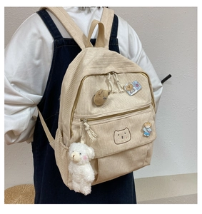 Detalle de mochila de pana beige con bordado de oso y colgante de peluche suave