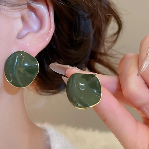 Detail of dark green irregular round earrings with 14k gold-plated edges on a model