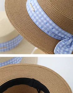 Close-up of flat top straw hat featuring blue plaid ribbon and golden metal logo tag