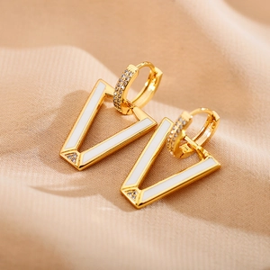 Detailed macro view of V-shaped gold earrings with white enamel and sparkling zircons