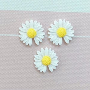 Three white resin daisy flower charms with yellow centers on a striped pastel background