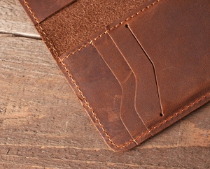 Detail of brown crazy horse leather wallet with stitching on vintage wood background