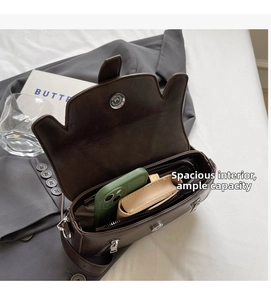 Detail view showing interior space of a dark brown saddle bag with zipper pocket and magnetic snap