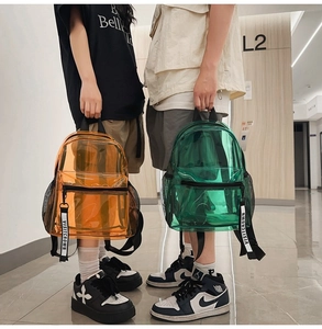 Detail of vibrant transparent PVC backpacks in bright orange and green with logo ribbons