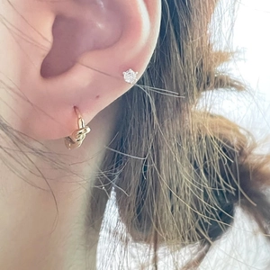 Detail shot of a knotted gold hoop earring and clear zircon stud worn on ear