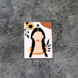 Macro shot of jewelry display card featuring floral woman illustration on concrete surface