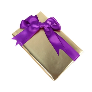 Gold metallic gift wrap paper with a purple satin ribbon bow on white background