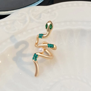 Dettaglio macro di anello a serpente dorato con cristalli verdi e perla bianca