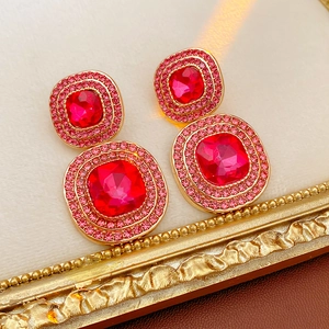 Detailed macro view of vintage gold square earrings with red gemstones and pink crystals