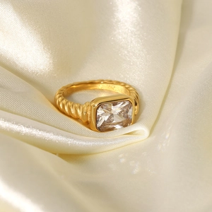 Detail of twisted gold ring featuring a square clear gemstone on beige silk fabric
