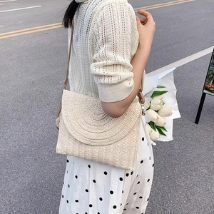 Elegante borsa a tracolla in paglia beige con patta e tracolla sottile indossata da modella
