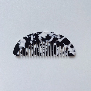 Detail of a portable mini black and white marble acetate hair comb with wide teeth
