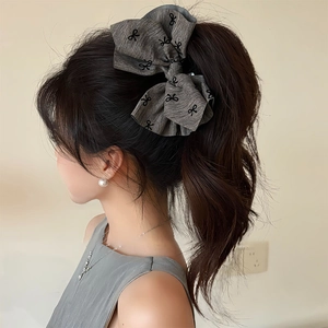 Close-up of a large grey fabric bow hair claw clip with black patterns on brown hair