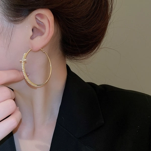 Détail d'une boucle d'oreille créole dorée avec pendentif croix en strass sur un mannequin