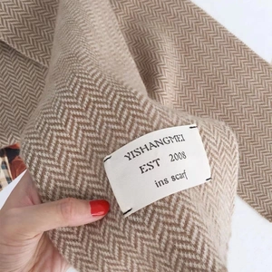 Gros plan sur l'écharpe en maille beige montrant le motif chevrons et l'étiquette blanche