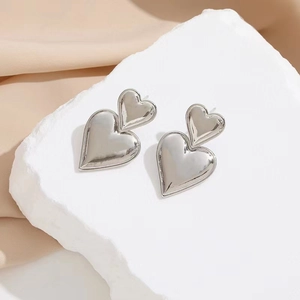 Polished silver stainless steel double heart drop earrings on a white marble display stand