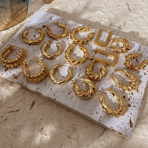 Gold plated chunky croissant hoop earrings and geometric studs on a stone tray