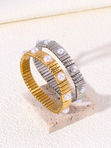Dettaglio di braccialetti con perle oro e argento su una base in travertino minimalista