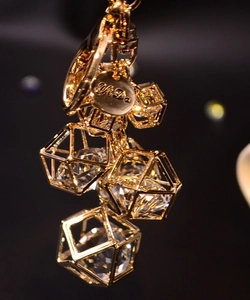 Close-up of golden geometric frame keychain with faceted crystal and branded charm tag