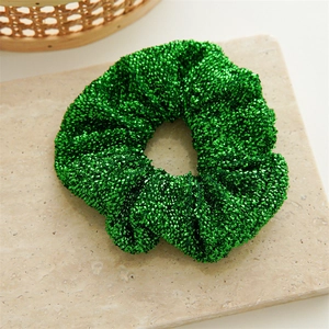 Detail of emerald green glitter scrunchie on beige marble background for Christmas