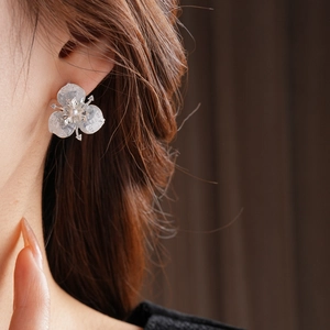 Close-up of elegant crystal flower earrings with silver accents and pearl on model