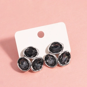 Dettaglio di orecchini geometrici in argento con tre zirconi grigio scuro su sfondo rosa