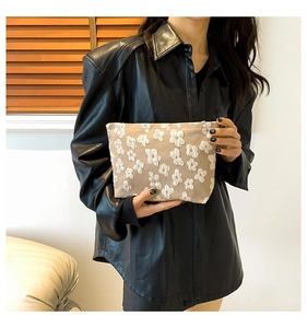 Close-up of beige clutch bag with 3D white flower pattern held by a model