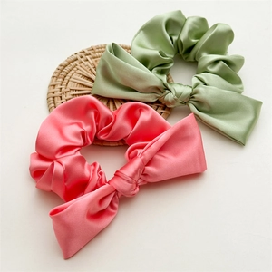 Green and pink satin scrunchies with bow design on a woven mat with white background