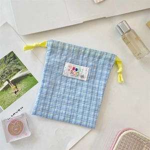 Blue plaid drawstring pouch for cosmetics shown with magazine and skincare items