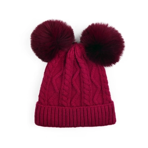 Détail du bonnet en maille torsadée bordeaux avec deux pompons doux en fausse fourrure