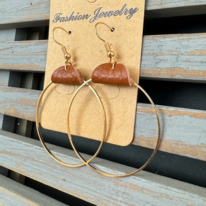 Elegant gold hoop earrings with brown leather accents on a rustic wooden background