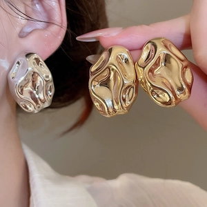 Close-up of irregular textured metal earrings in gold and silver lava style