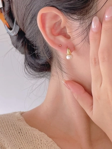 Close-up of minimalist gold pearl hoop earrings worn by a model in a cozy knit sweater