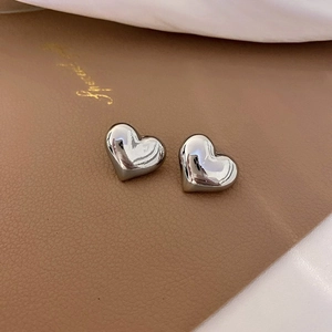 Macro shot of silver minimalist heart-shaped stud earrings on a textured leather background