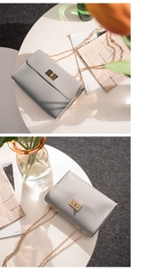 Detail of grey chain crossbody bag with golden rectangular lock on minimalist desk