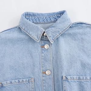 Detail of light blue denim shirt showing collar, metal buttons and stitching texture