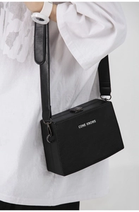 Detail of the black leather box bag with wide strap and white CONE KNOWS lettering